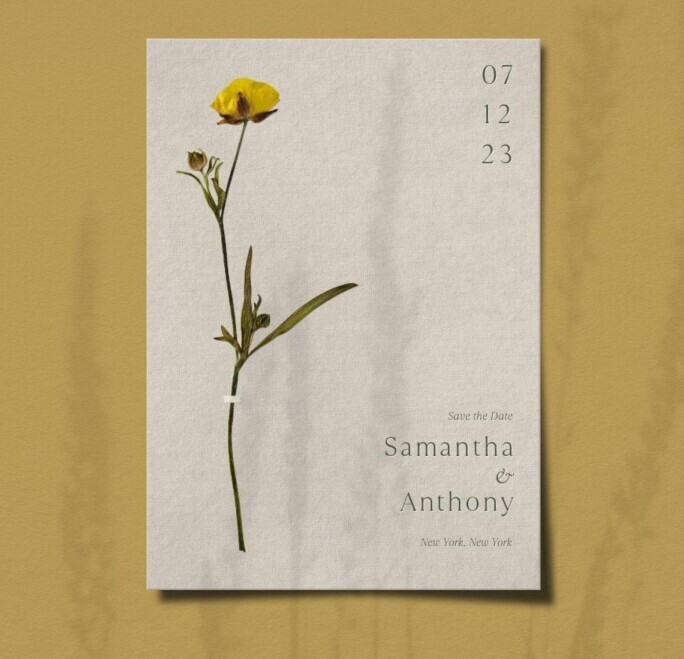 Bliss & Bone botanical save the date template with pressed yellow buttercup on linen-textured cream card stock, stacked date numerals and elegant serif typography in warm gray