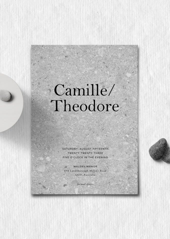 An overhead view of a gray wedding invitation for a couple named Camille and Theodore