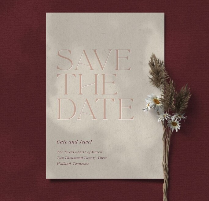 Bliss & Bone minimalist save the date card on textured cream stock with blush serif typography, styled with dried pampas grass and daisies against a deep burgundy background